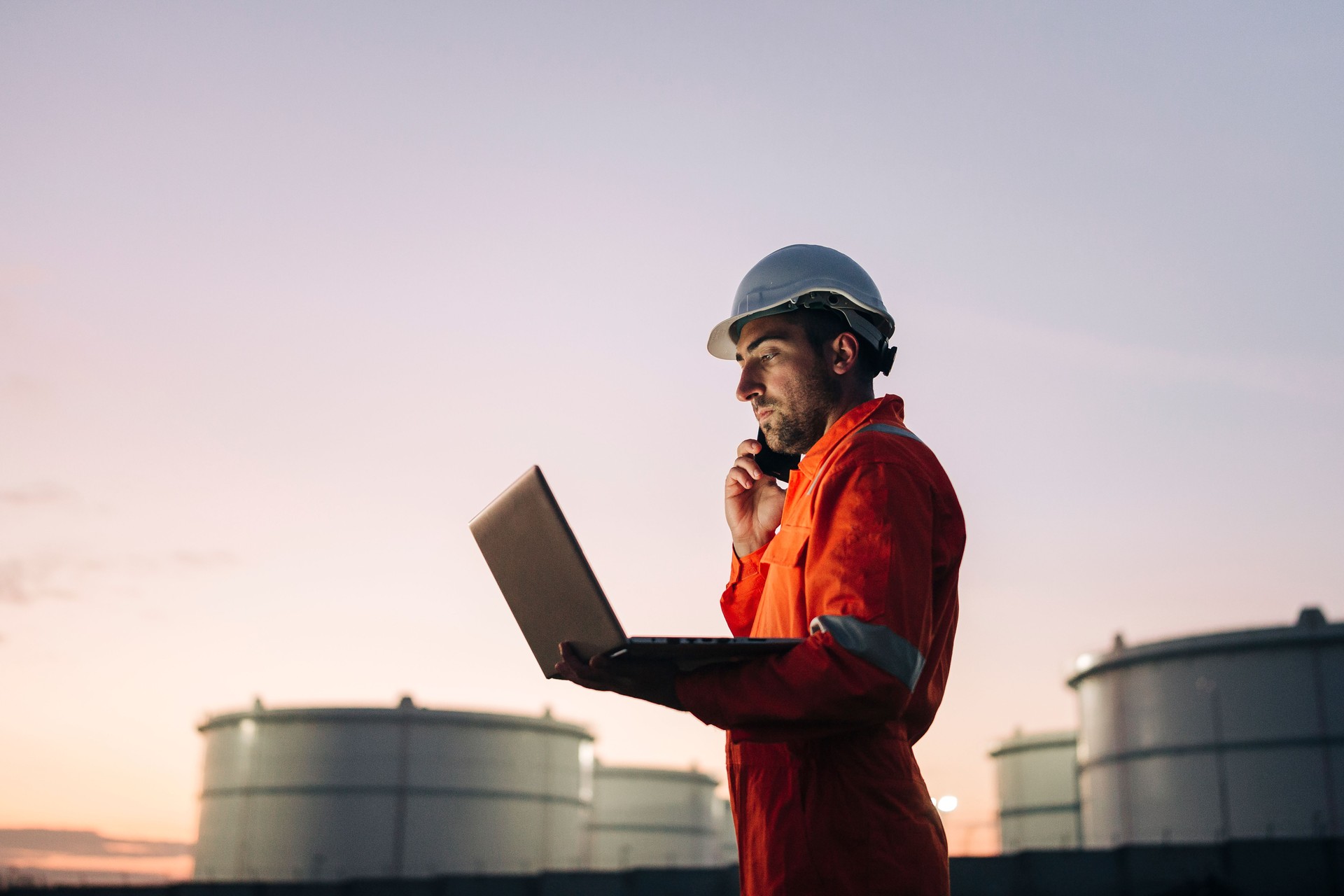Engineer using laptop near oil refinery at night